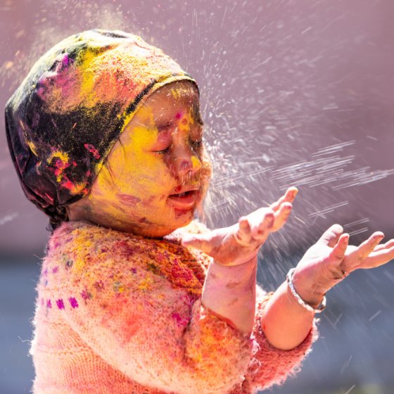 Baby bedekt met natuurlijke schmink spelend met een waterstraal