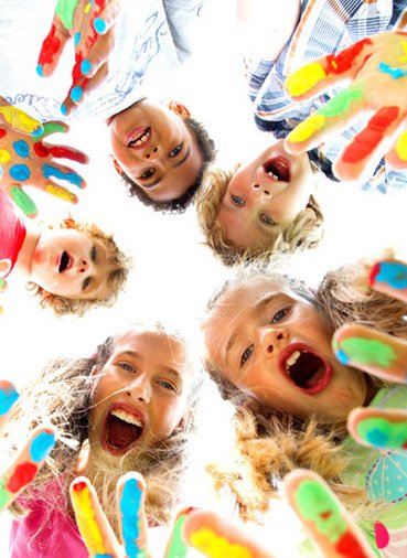 Five children in a circle with their heads down, their hands covered in paint and laughing like crazy