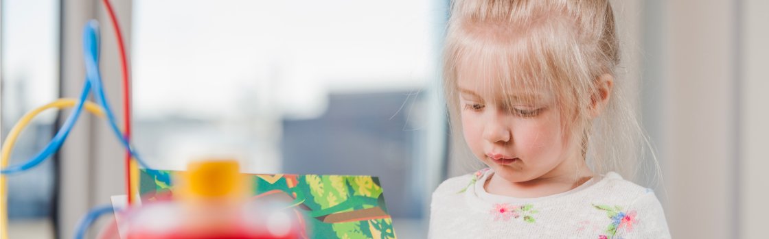 Jeune enfant blonde, dans un lieu d'accueil, lisant un livre d'histoires